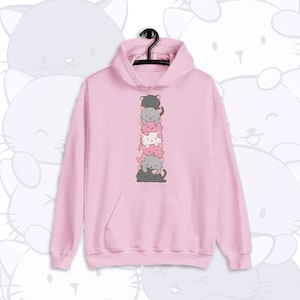 May include: A light pink hoodie with a stacked cat graphic. The graphic features a vertical stack of six cartoon cats in various shades of gray, pink, and white. The hoodie has a front pocket and a hood.