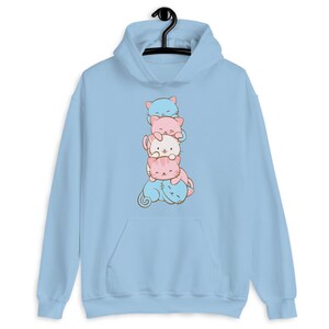 May include: A light blue hoodie with a stack of four cartoon cats in different colors. The cats are stacked on top of each other, with the largest cat at the bottom and the smallest cat at the top. The cats are all smiling and have big eyes.