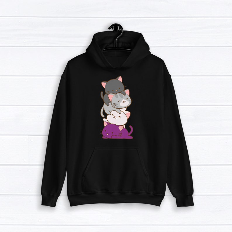Puede incluir: Sudadera con capucha negra con una pila de cuatro gatos de dibujos animados impresos en la parte delantera. Los gatos est&aacute;n apilados de mayor a menor, siendo el gato de abajo morado, el siguiente blanco, el siguiente gris y el gato de arriba negro.