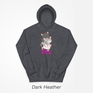 Puede incluir: Sudadera con capucha de color gris oscuro jaspeado con una pila de cuatro gatos de dibujos animados en la parte delantera. Los gatos est&aacute;n apilados uno encima del otro, con el gato de abajo de color morado, el siguiente de color blanco, el siguiente de color gris y el gato de arriba de color negro. Todos los gatos tienen la nariz rosa y bigotes.