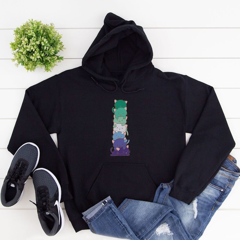 K&ouml;nnte beinhalten: Schwarzer Hoodie mit einem Stapel von f&uuml;nf bunten Comic-Katzen auf der Vorderseite. Die Katzen sind &uuml;bereinander gestapelt und in einem Regenbogen-Farbschema gehalten. Der Hoodie ist ein bequemes und stylisches Kleidungsst&uuml;ck.