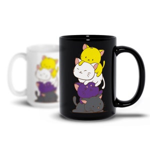 Puede incluir: Taza de cerámica negra con un diseño de gatos de dibujos animados apilados en amarillo, blanco, morado y gris. Una segunda taza blanca borrosa con el mismo diseño está en el fondo. La taza tiene un asa grande y curvada.