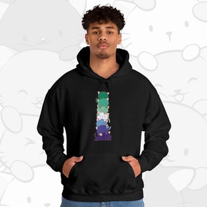 K&ouml;nnte beinhalten: Ein schwarzer Hoodie mit einem Aufdruck von sechs bunten Comic-Katzen, die auf dem Vorderteil &uuml;bereinander gestapelt sind. Die Katzen sind vertikal &uuml;bereinander gestapelt, wobei die unterste Katze lila, die n&auml;chste blau, dann wei&szlig;, gr&uuml;n und schlie&szlig;lich eine gr&uuml;ne Katze oben ist.