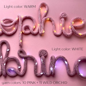 May include: Two cursive words crafted from pink knitted yarn, illuminated by integrated string lights. The top word features warm-toned lights, while the bottom word features white lights. Text includes Light color: WARM, Light color: WHITE, and yarn colors: 10 PINK + 11 WILD ORCHID.