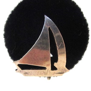May include: A silver sailboat pin with a cut-out design. The pin is on a black background.