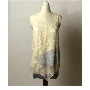 May include: A white lace tank top with a delicate floral design and a layered, asymmetrical hem.