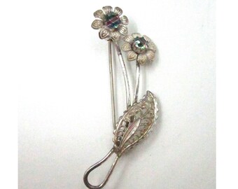 May include: Silver filigree brooch with two flowers and a leaf. The flowers have iridescent centers.
