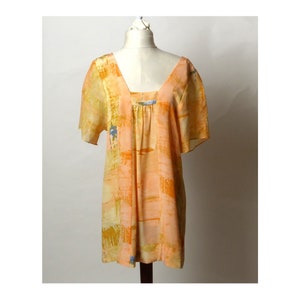 Puede incluir: Una blusa holgada de manga corta con cuello cuadrado. La blusa est&aacute; hecha de una tela ligera y presenta un estampado abstracto en tonos naranja, amarillo y azul.