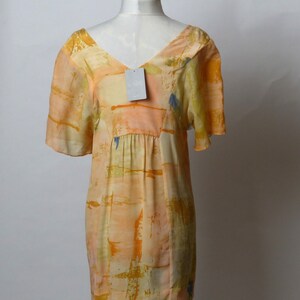 Puede incluir: Un vestido corto sin mangas con escote en V y estampado abstracto en tonos naranja, amarillo y azul. El vestido tiene una cintura fruncida y una silueta fluida.