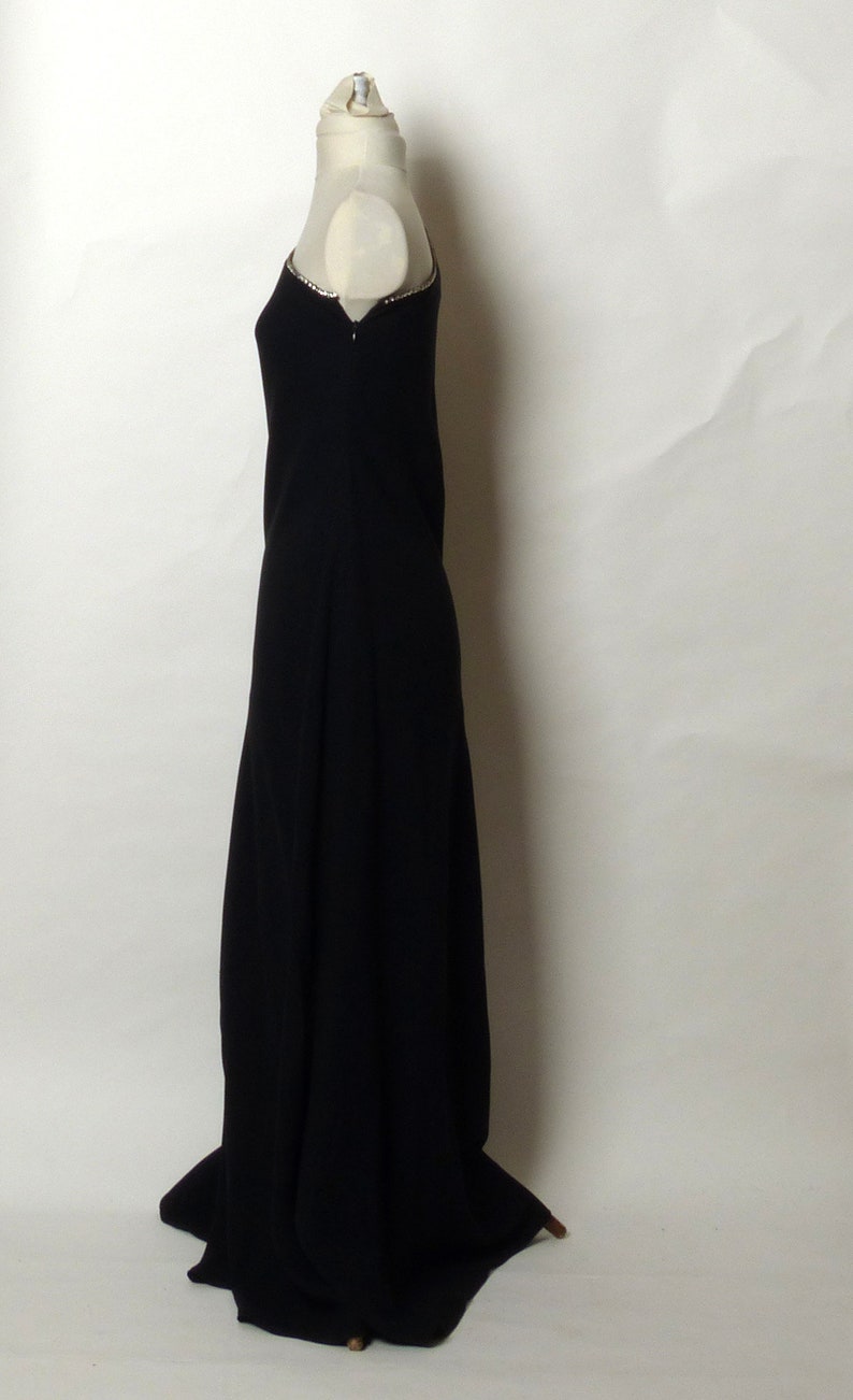 May include: A black floor-length dress with a beaded neckline. The dress is on a white mannequin.