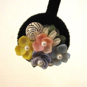 May include: A black velvet hair accessory with a cluster of seashell flowers and a striped seashell. The flowers are yellow, pink, and blue, each with a pearl centre. A unique, handcrafted hair accessory.