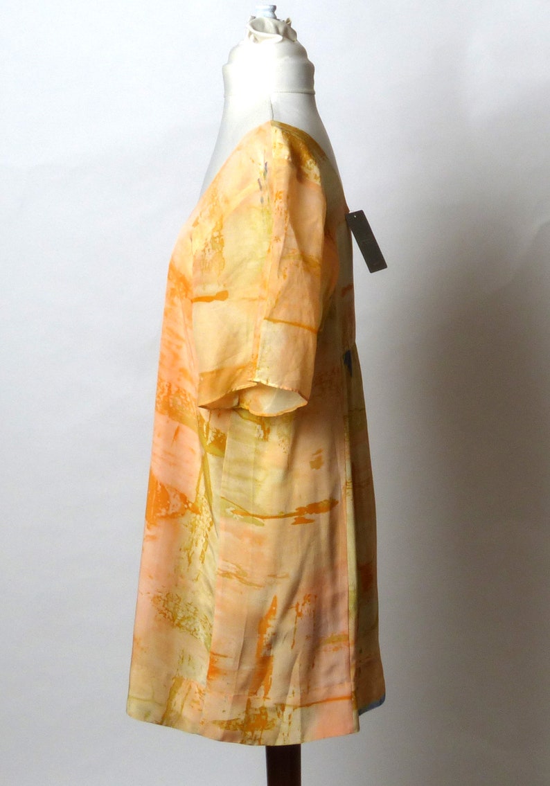 Puede incluir: Un vestido de manga corta con estampado abstracto en melocot&oacute;n y amarillo. El vestido tiene un escote en V y un corte holgado.