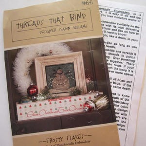 May include: A craft pattern booklet titled Threads That Bind #641 by Shawn Williams, featuring a snowman illustration in a wooden frame, a white wreath, and glass Christmas tree ornaments. The text includes instructions for punchneedle embroidery.