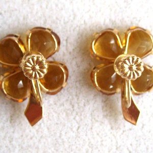 May include: A pair of gold tone earrings with four-leaf clover designs. Each clover is made of amber colored glass.