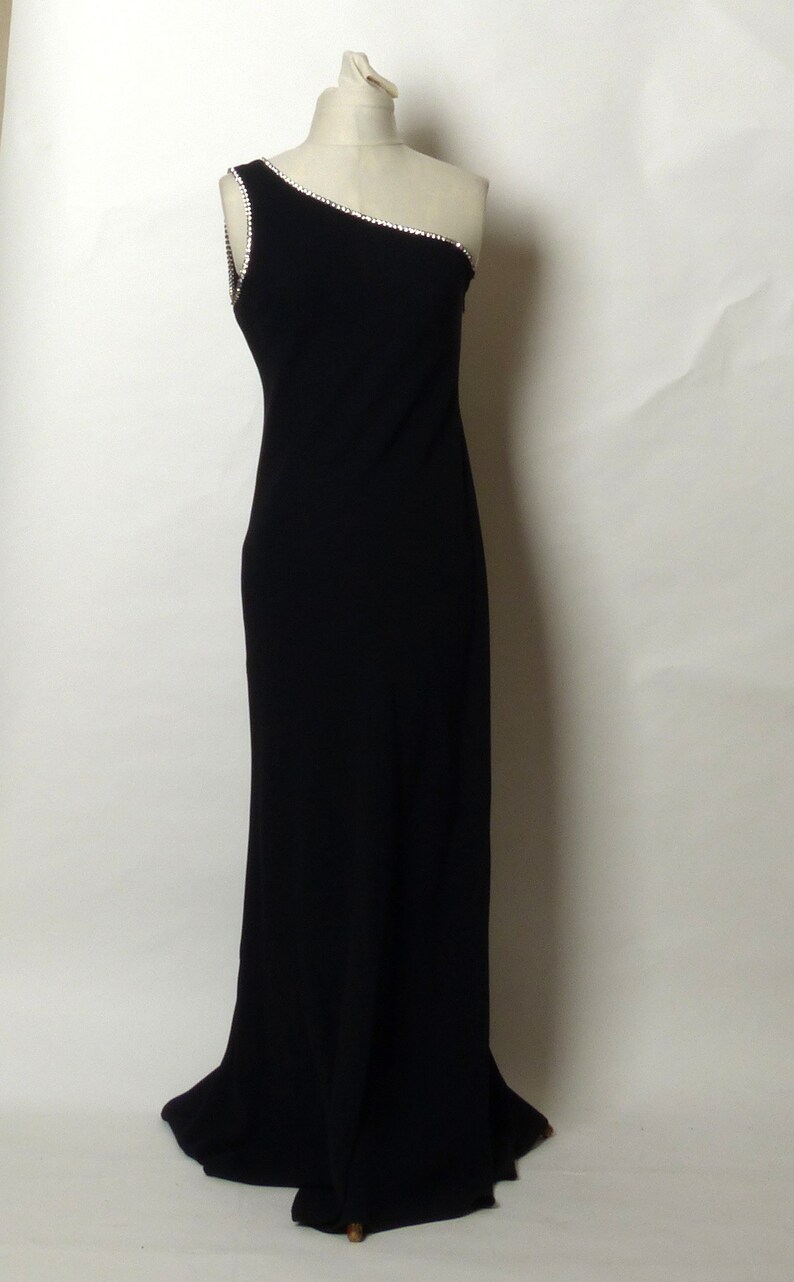 May include: A black one-shoulder evening gown with a beaded trim. The gown has a fitted bodice and a flowing skirt.