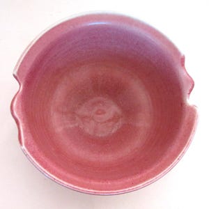 Może przedstawiać: Ręcznie robiona ceramiczna miska z unikalnym, falistym wzorem obręczy. Misa ma gradient różowych i fioletowych odcieni, z jaśniejszą różową obręczą. Ta dekoracyjna miska jest idealna do serwowania lub jako element dekoracyjny.