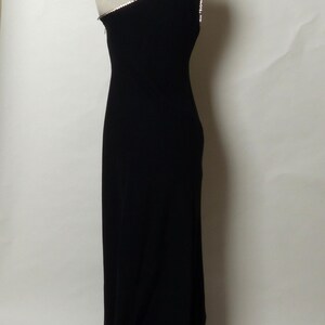 May include: A black one-shoulder evening gown with a rhinestone trim along the neckline.