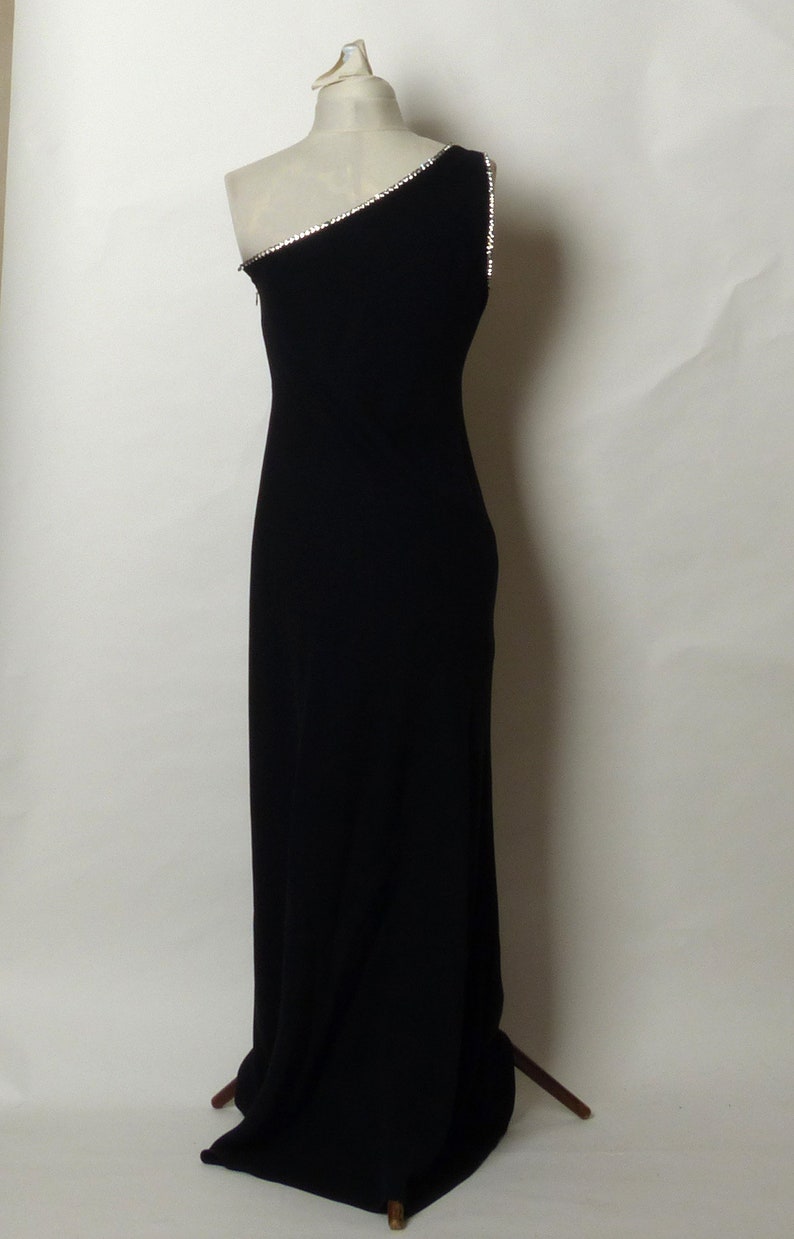 May include: A black one-shoulder evening gown with a rhinestone trim along the neckline.