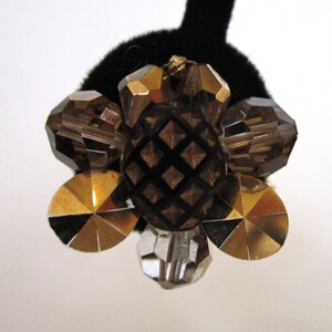 May include: A gold and brown flower-shaped brooch with a textured centre and faceted glass stones.