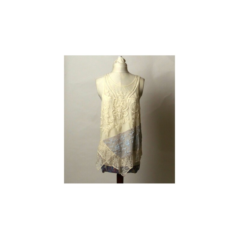May include: A white lace tank top with a delicate floral design and a layered, asymmetrical hem.