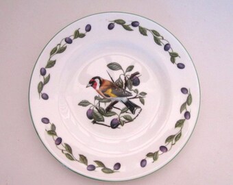 May include: White ceramic plate with a green rim, featuring a detailed illustration of a colorful bird perched on a branch with purple plums. The plate is decorated with a repeating pattern of plums and leaves.