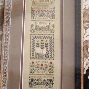 Peut inclure: Un sampler de point de croix encadré avec une maison et des fleurs. Le texte dit : "prairie brome, humilité, mauve sauvage, confort, marguerite, innocence, gaillardia, variété, chardon des champs, austérité, trèfle des prés, amitié."