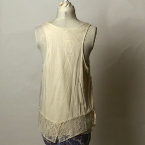 May include: A white sleeveless top with a lace trim. The top is on a white mannequin.