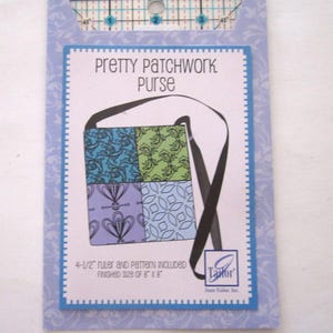 Puede incluir: Un patrón de costura para un "Pretty Patchwork Purse" con una regla de 4,5 pulgadas incluida. El tamaño final del bolso es de 20,3 cm x 20,3 cm. El diseño presenta una ilustración de bolso con cuatro cuadrados estampados en azul, verde y morado.