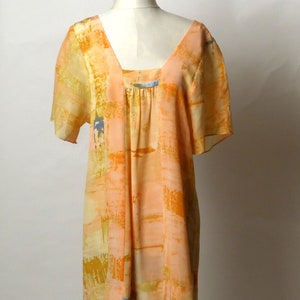 Puede incluir: Un vestido corto de manga corta, holgado, con cuello redondo y fondo de color melocot&oacute;n. El vestido tiene un patr&oacute;n geom&eacute;trico en tonos de naranja, amarillo y azul.