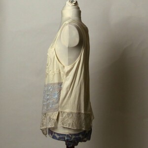 May include: A sleeveless, off-white top with a lace trim and floral embroidery. The top is made of a lightweight fabric and has a relaxed fit.