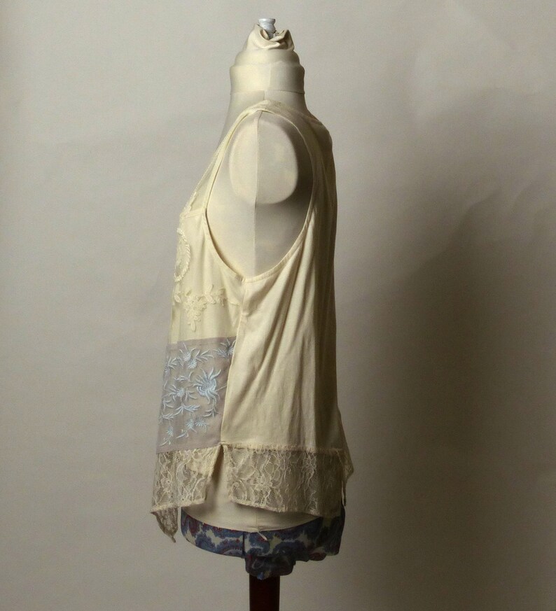 May include: A sleeveless, off-white top with a lace trim and floral embroidery. The top is made of a lightweight fabric and has a relaxed fit.