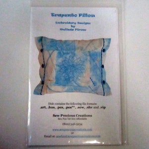 Pode incluir: Um cartão branco com texto azul que diz "Trapunto Pillow Embroidery Designs by Melinda Pirone". O cartão mostra um travesseiro azul e branco com um desenho bordado azul no centro. O cartão também inclui informações sobre os formatos de arquivo incluídos no disco e as informações de contato da Sew Precious Creations.