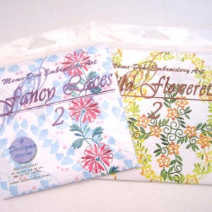 May include: Two sealed packages of embroidery art designs. One package features the text "Fancy Laces" with floral illustrations in pink and blue. The other package has "Wild Flowerets" with a floral wreath design.
