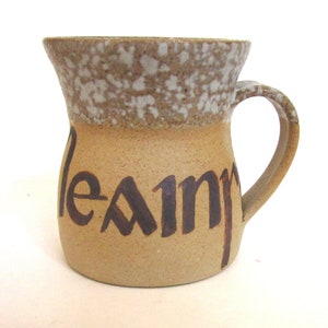 Puede incluir: Una taza de cerámica marrón con un esmalte moteado y una asa marrón. La taza tiene la palabra "leann" escrita en ella con letras marrones.