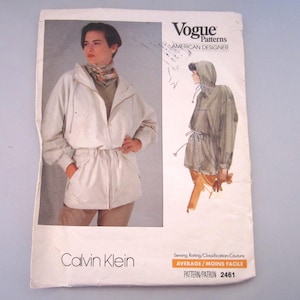 May include: A Vogue Patterns American Designer sewing pattern envelope for a Calvin Klein jacket, pattern number 2461. The front features a photograph of a person wearing a light-coloured hooded jacket with a drawstring waist and a line drawing illustration.