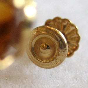 May include: Close-up of a gold earring with a 14k marking. The earring has a round back and a decorative front.