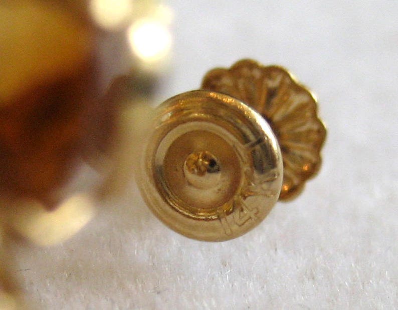 May include: Close-up of a gold earring with a 14k marking. The earring has a round back and a decorative front.
