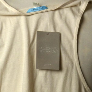 May include: A cream-colored sleeveless top with a scoop neck and a tag that reads "Anthropologie" in a decorative font.