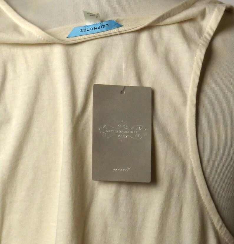 May include: A cream-colored sleeveless top with a scoop neck and a tag that reads "Anthropologie" in a decorative font.