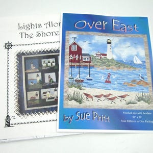 May include: Two quilt pattern booklets titled Lights Along The Shore and Over East by Sue Pritt. The Over East cover features a coastal scene with a lighthouse, red buildings, sailboats, and birds on a beach, noting a finished size of 36 inches by 36 inches.