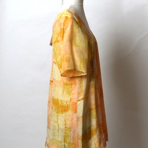 Puede incluir: Un vestido de manga corta con estampado naranja y amarillo con escote en V. El vestido est&aacute; hecho de una tela ligera y tiene un corte holgado.