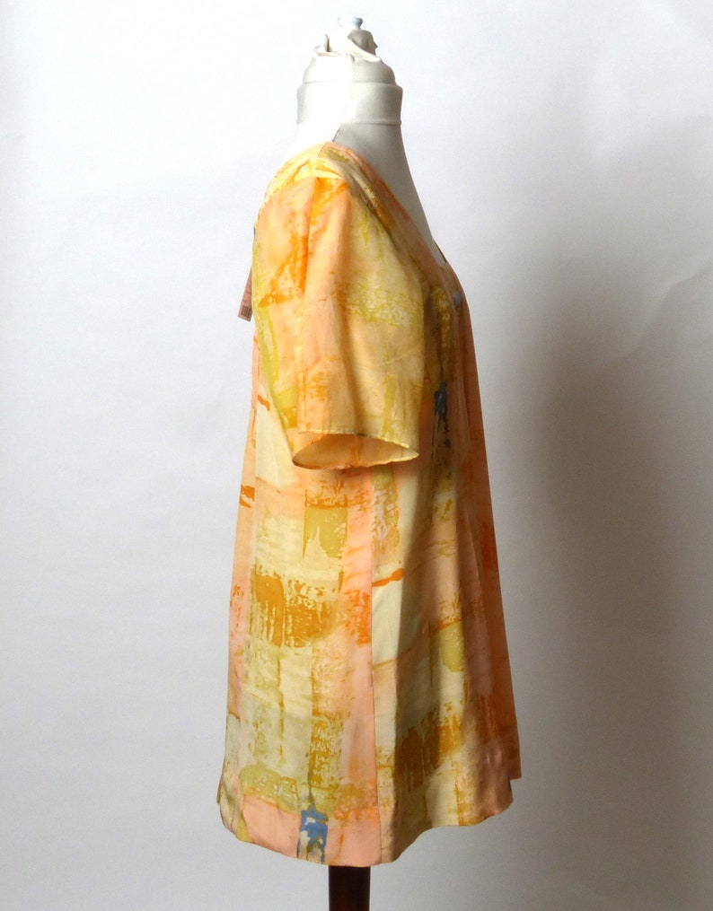 Puede incluir: Un vestido de manga corta con estampado naranja y amarillo con escote en V. El vestido est&aacute; hecho de una tela ligera y tiene un corte holgado.