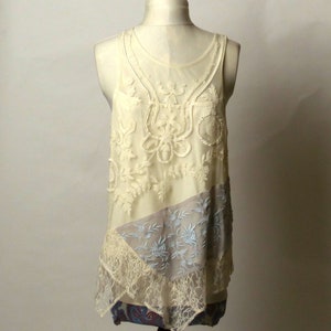 May include: A white lace tank top with a layered design. The top has a delicate floral pattern and a sheer overlay. The bottom layer is a light gray fabric with a floral pattern.