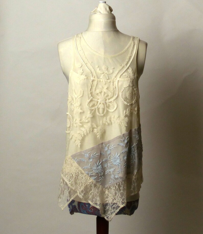 May include: A white lace tank top with a layered design. The top has a delicate floral pattern and a sheer overlay. The bottom layer is a light gray fabric with a floral pattern.