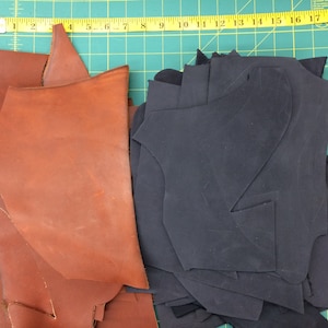 May include: A pile of brown leather scraps and a pile of black leather scraps. The leather scraps are on a green cutting mat.