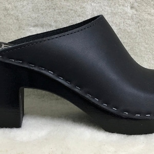 May include: Black leather heeled clogs with a thick platform sole and a stitched seam around the top edge.