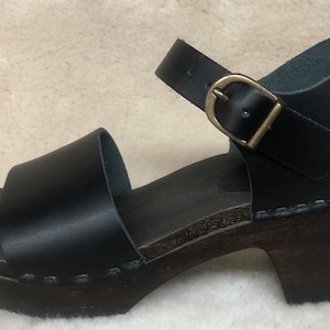 May include: Black leather heeled sandals with a wooden platform and an adjustable ankle strap with a gold buckle.