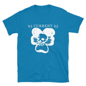 以下が含まれることがあります： 白い文字で「93 CURRENT 93」と書かれたターコイズ色のTシャツ。白い花の形の中に頭蓋骨のグラフィックがあります。柔らかい素材で作られたシャツです。