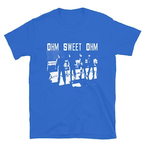 Puede incluir: Camiseta azul real con el texto blanco "OHM SWEET OHM". Debajo, un gráfico blanco de una banda actuando en un escenario. La camiseta está hecha de un material suave.