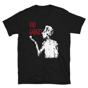 May include: Black t-shirt featuring a white graphic of a figure blowing something from their hand. The text "FAD GADGET" is printed in red above the figure.
